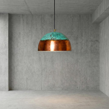 Pendant light with copper and teal design hanging in a concrete room.