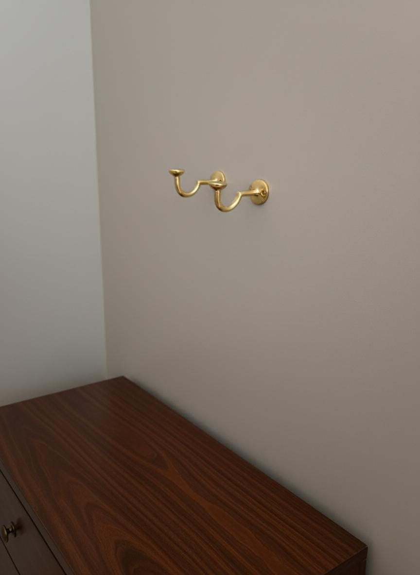 Gold wall hook on a plain wall above a wooden surface