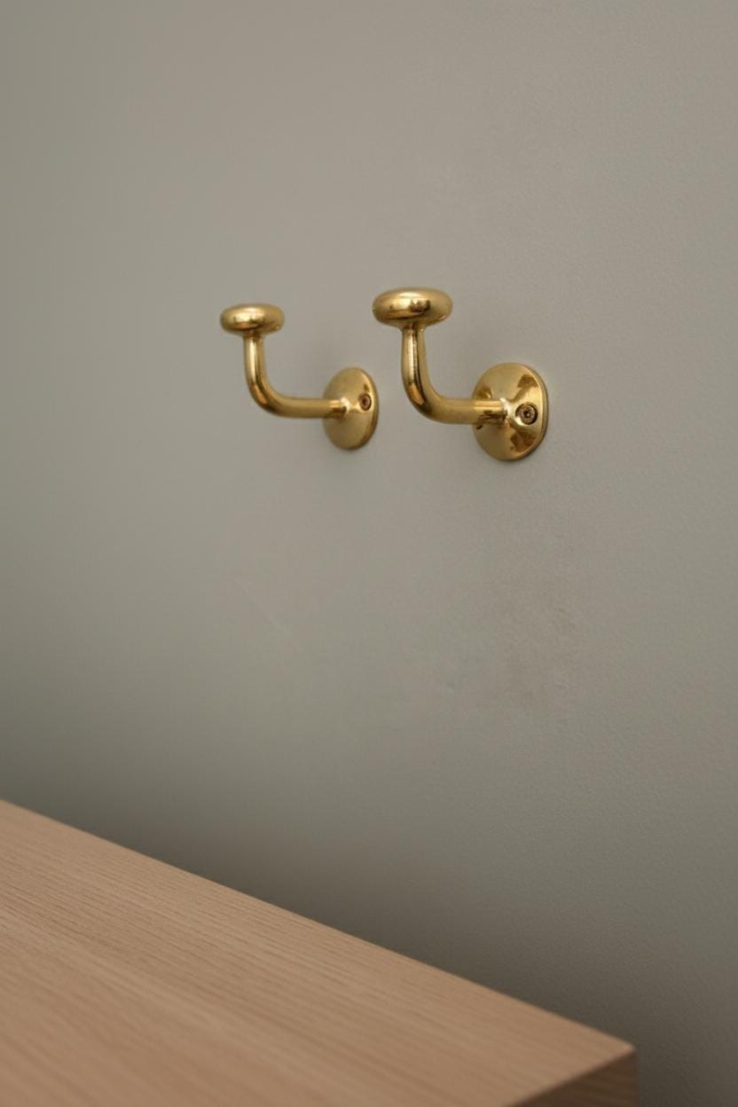 Two gold wall hooks on a plain wall with a wooden surface in the foreground.
