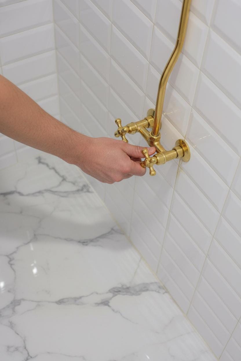 Hand adjusting a gold faucet in a bathroom with marble floor and tiled wall.