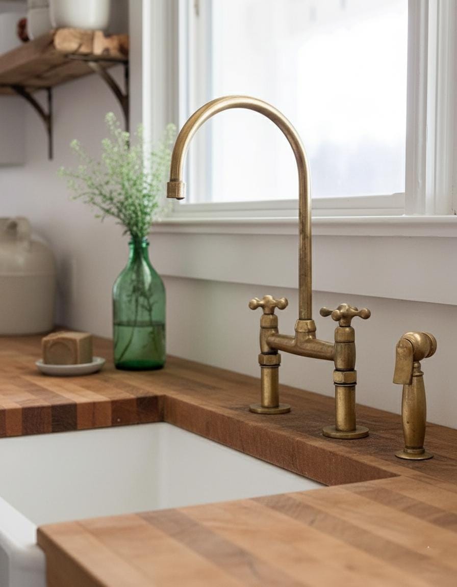 Brass kitchen faucet and handles on a wooden countertop with a window in the background.