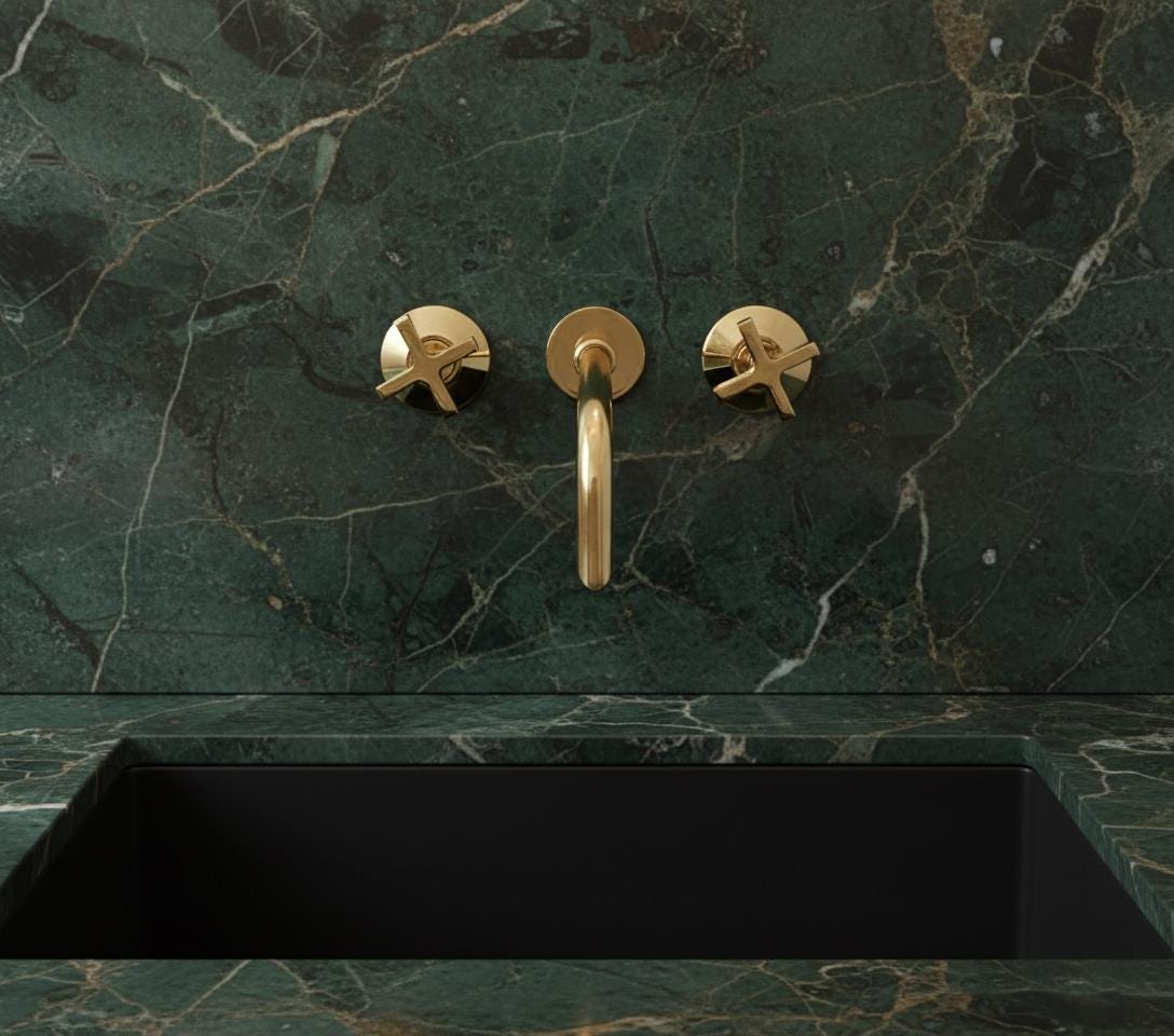 Gold faucet and handles on a green marble wall with a black sink below.