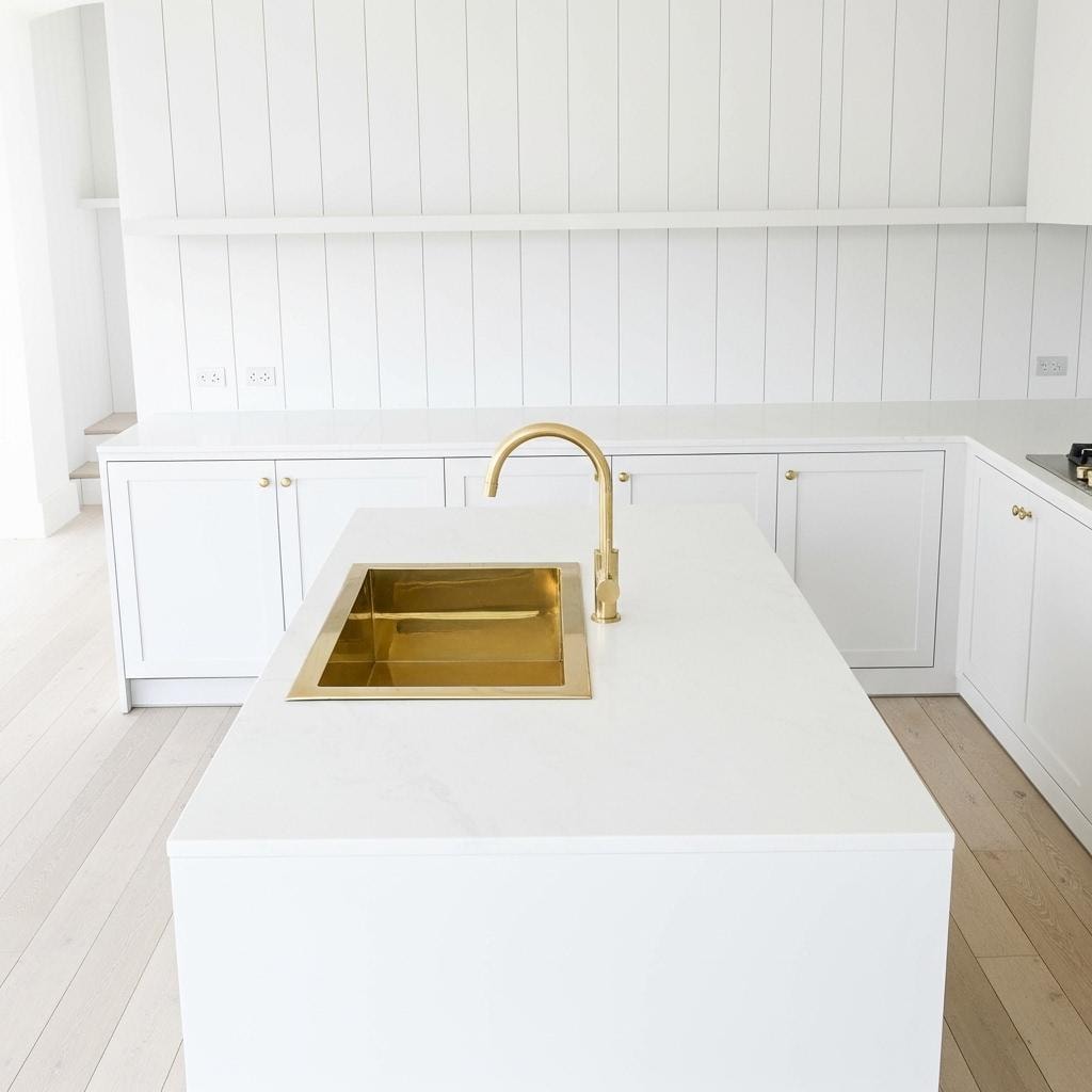 Modern kitchen with white cabinetry, gold faucet, and island.
