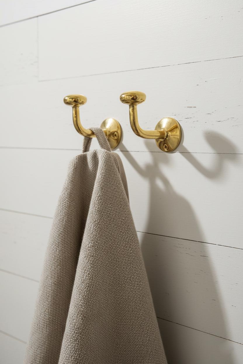 Gold towel hook with a beige towel on a white wooden wall