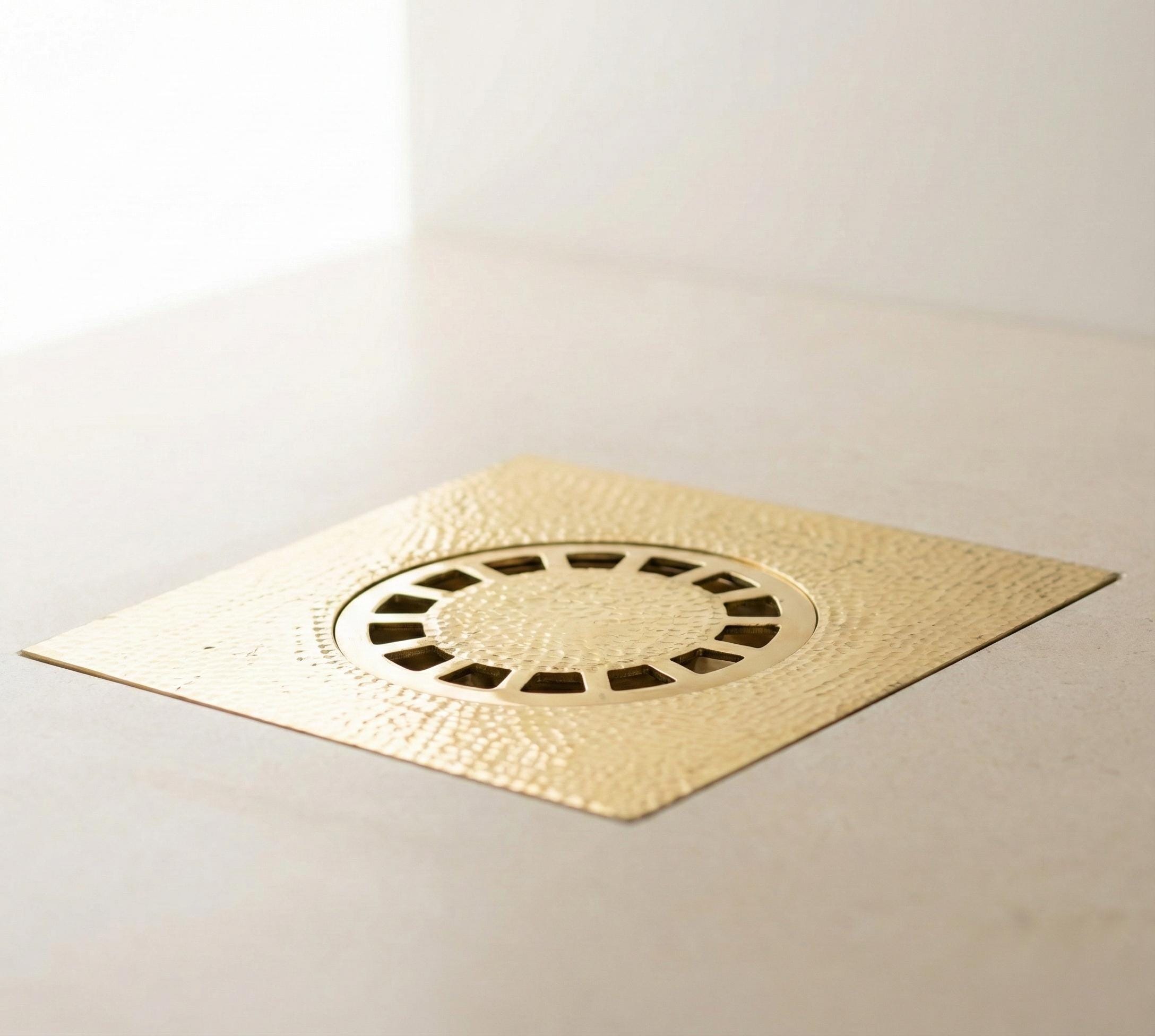Gold-colored brass floor drain cover on a light gray background