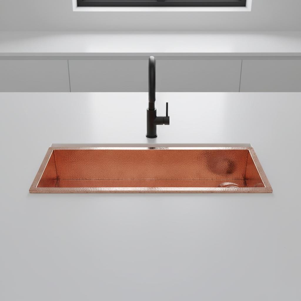 Copper kitchen sink with black faucet on a gray countertop