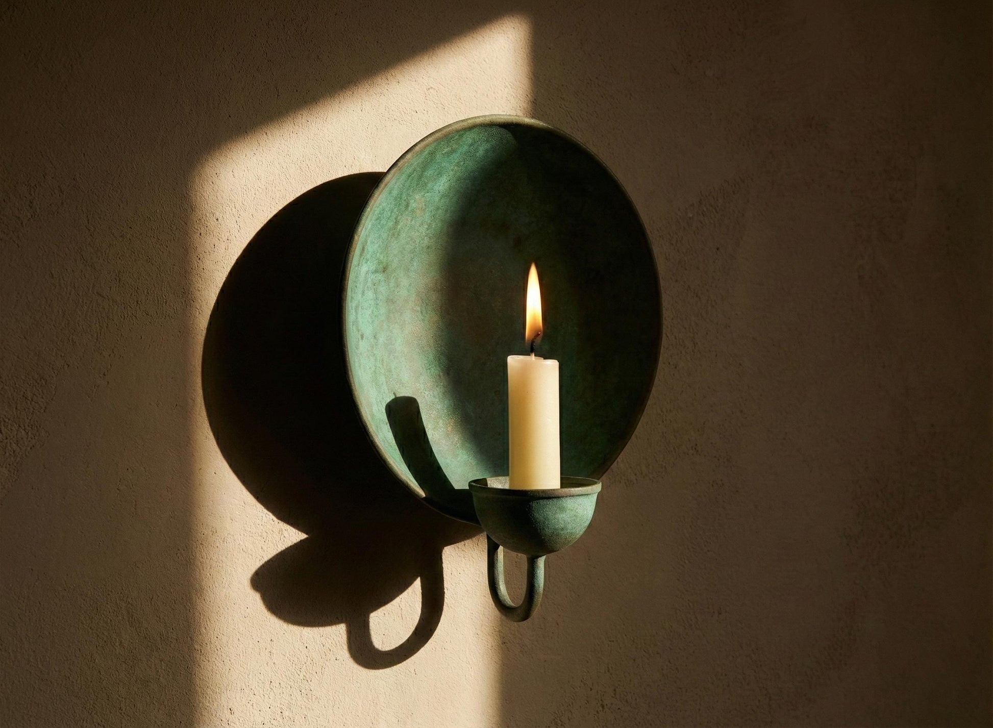 Green wall sconce with a lit candle against a dark wall