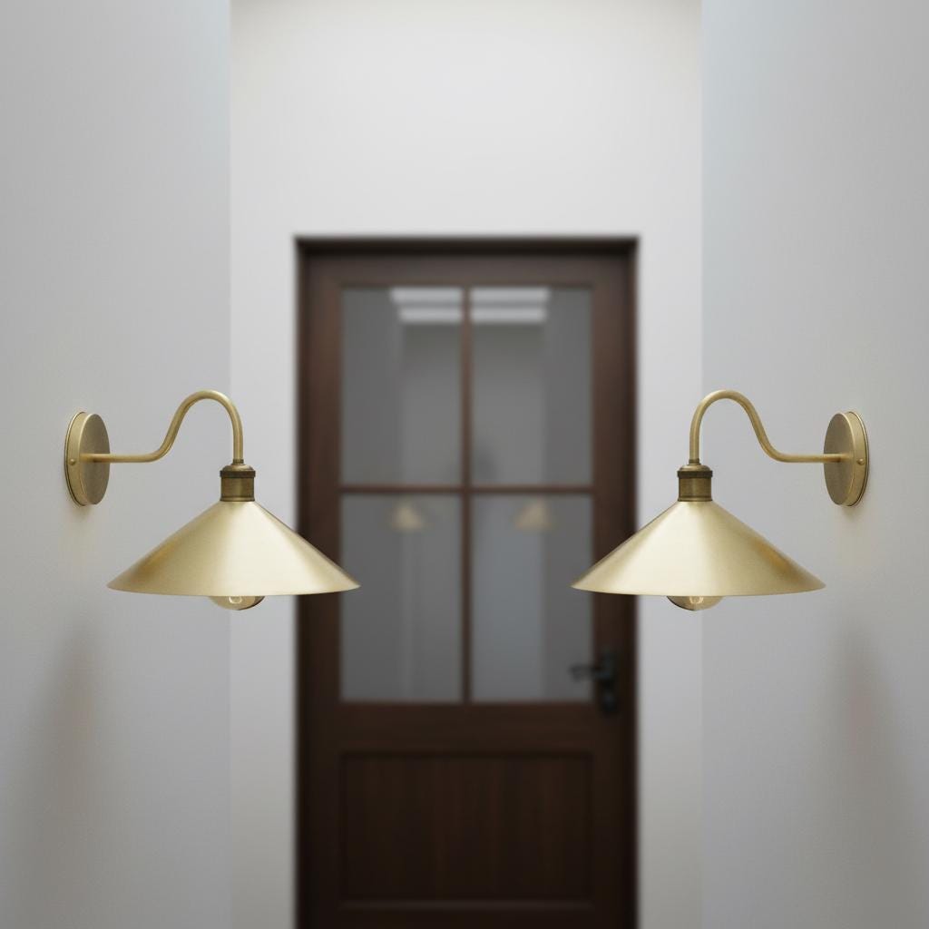 Two gold wall sconces on a white wall with a door in the background.