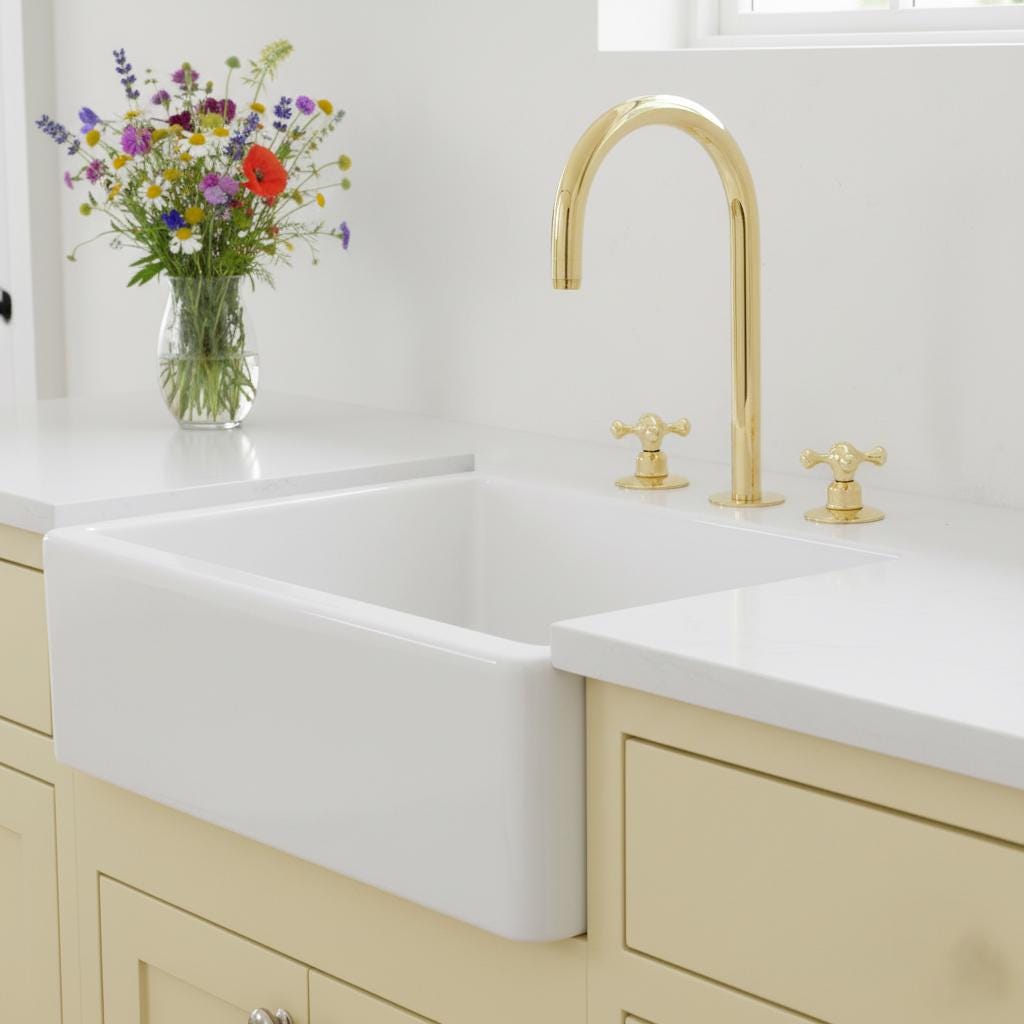 Kitchen sink with gold faucet and vase of flowers on white countertop