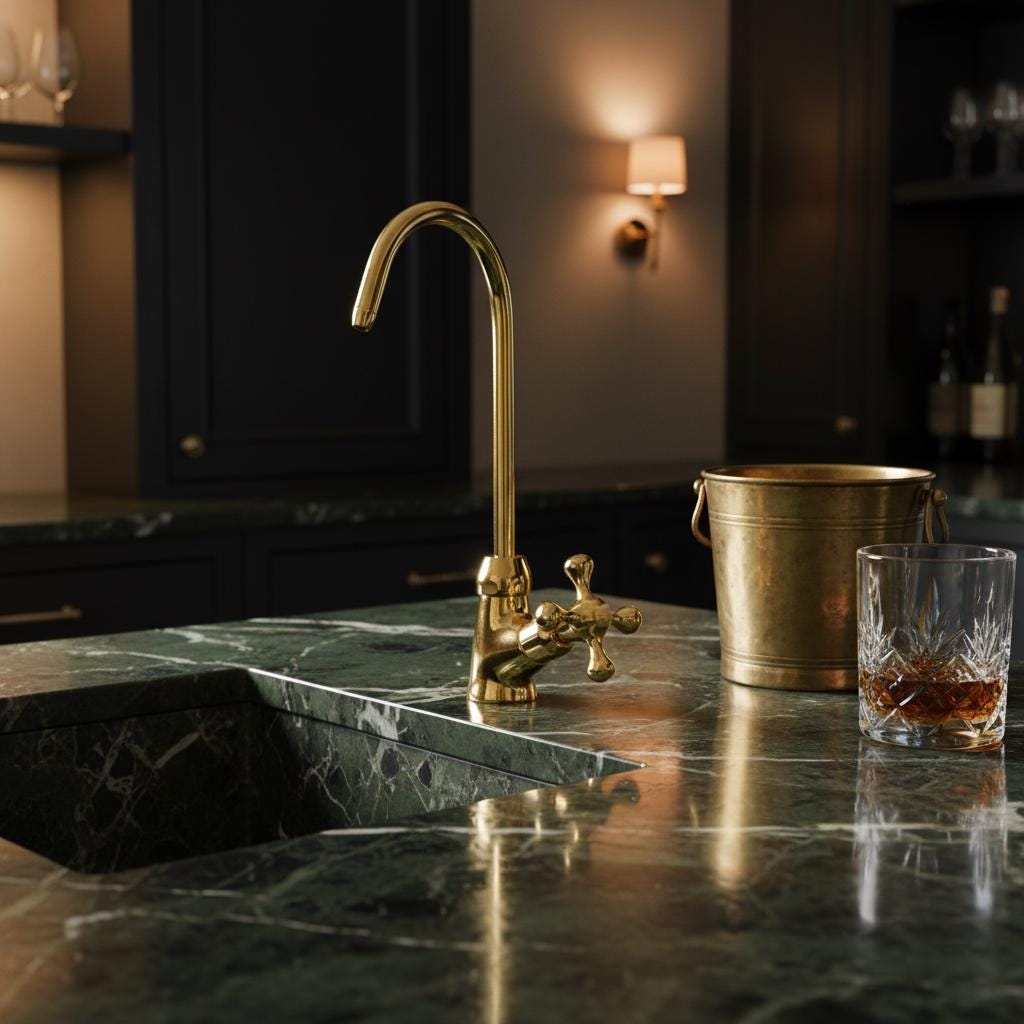 Gold faucet on a marble countertop with a glass of whiskey and a bucket.