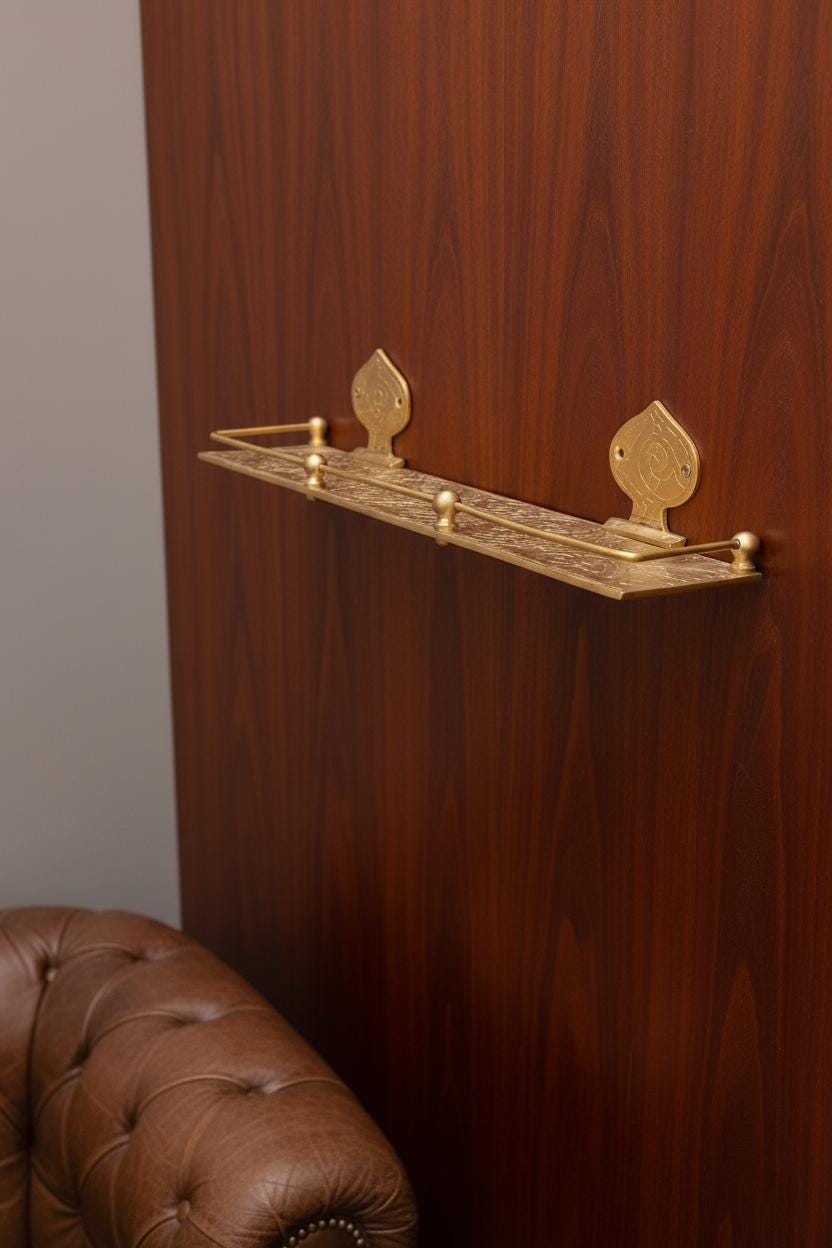 Decorative gold shelf mounted on a wooden wall with a brown leather couch in the foreground.