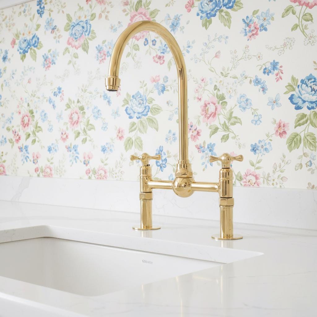 Gold kitchen faucet on a white countertop with floral wallpaper in the background