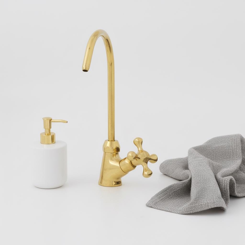 Gold kitchen faucet with a white soap dispenser and gray towel on a light gray background