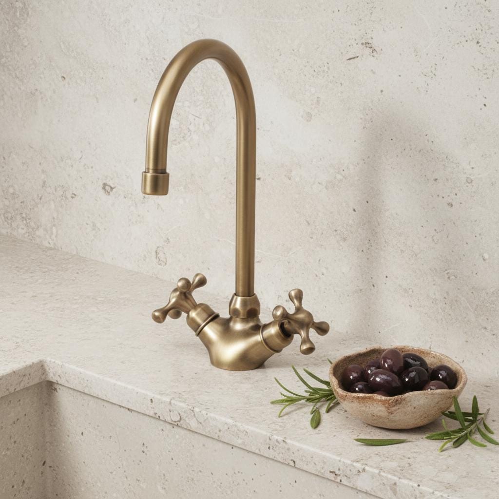 Brass kitchen faucet on a light stone countertop with a bowl of olives and rosemary.
