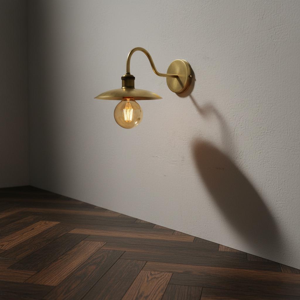 Wall-mounted brass lamp casting a shadow on a white wall with wooden floor.