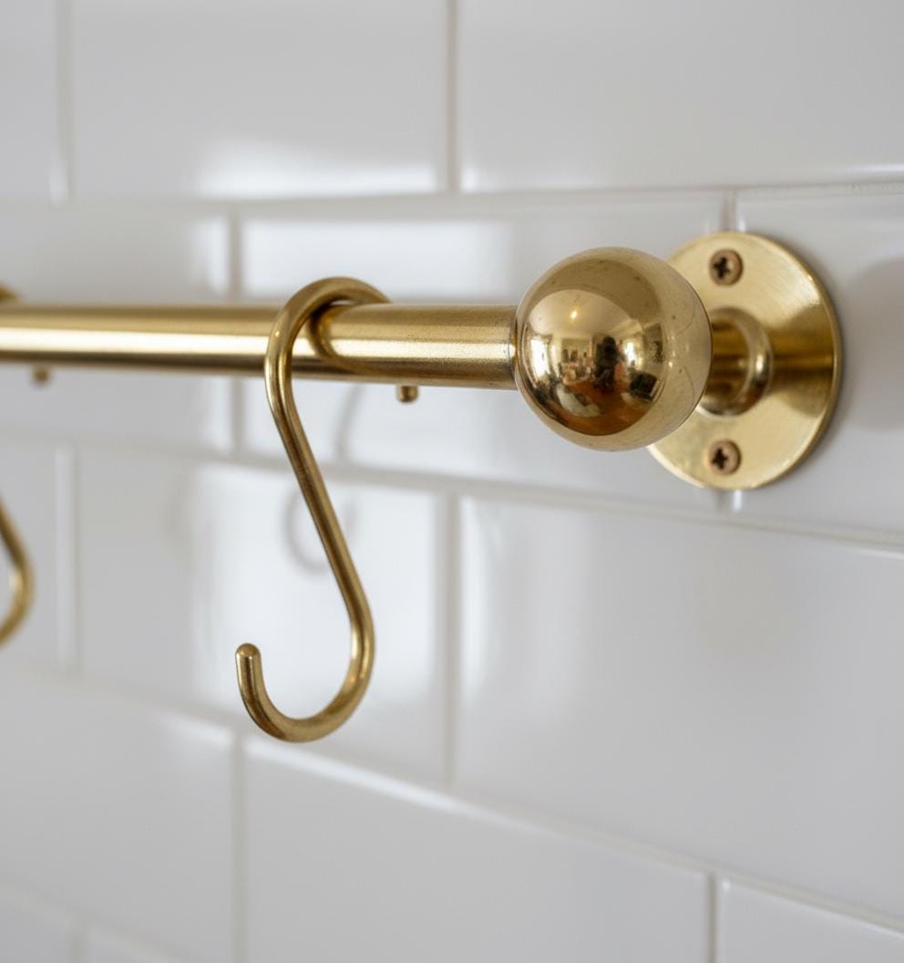 Gold shower curtain rod with bracket on a white tiled wall