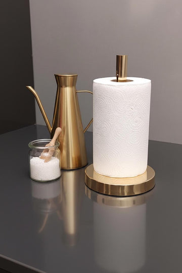 Gold paper towel holder with a roll of paper towels on a reflective surface.