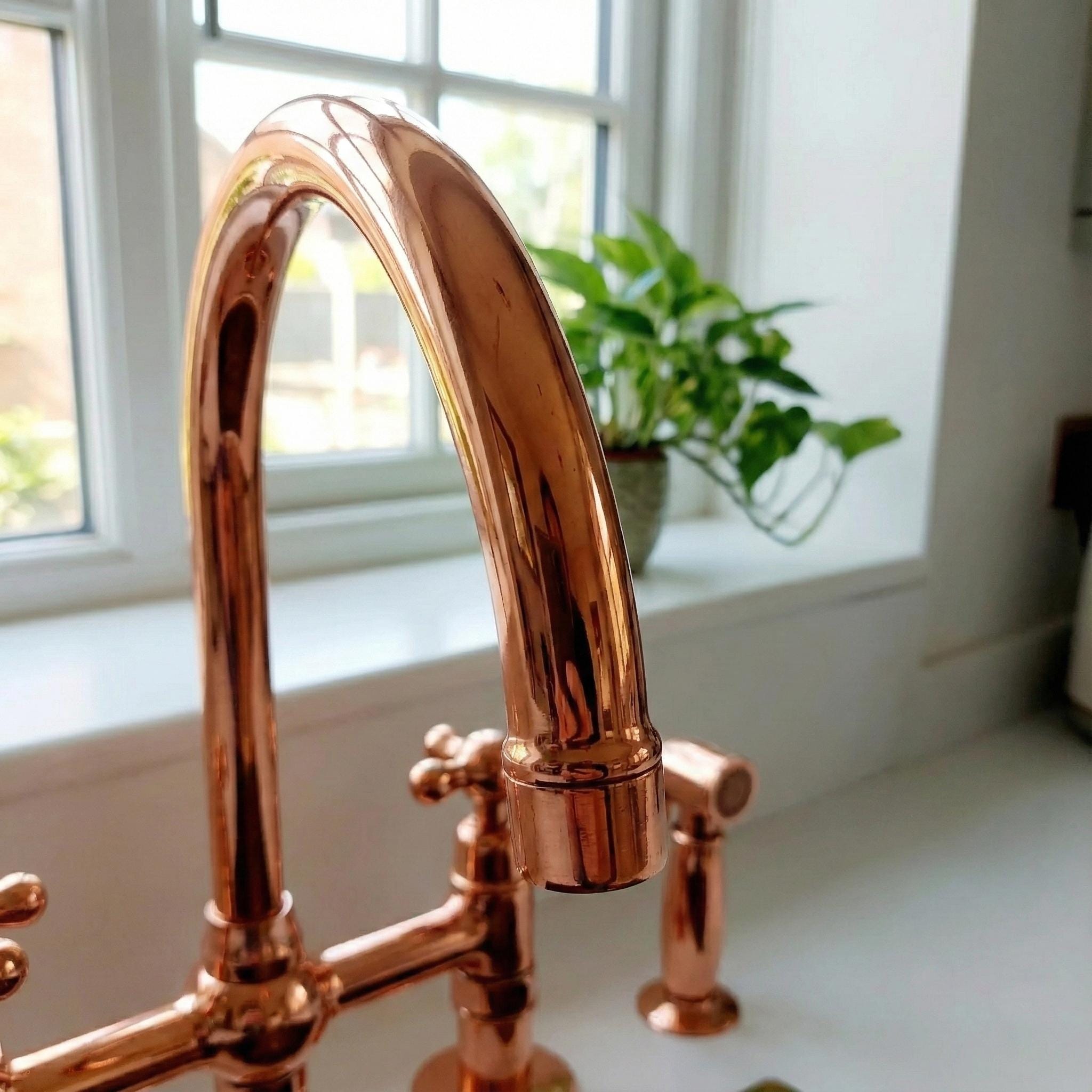 Rose gold faucet on a kitchen sink with a window and plant in the background