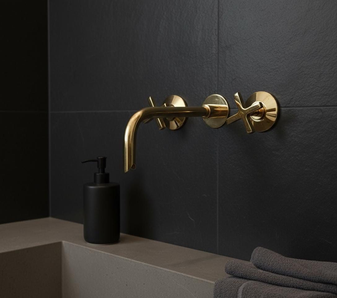 Gold faucet on a black tiled wall with a black soap dispenser and gray towels.