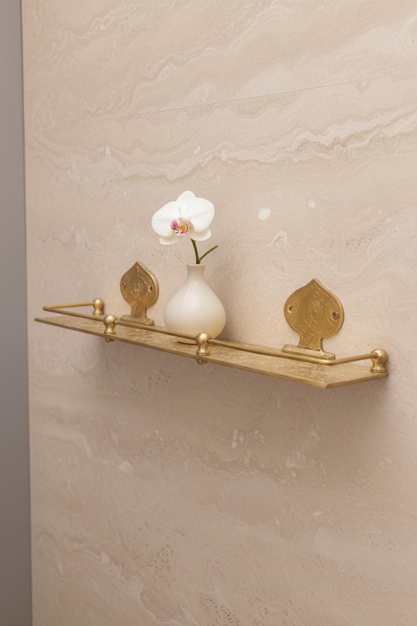 Gold decorative shelf with a white vase and flower against a beige wall.