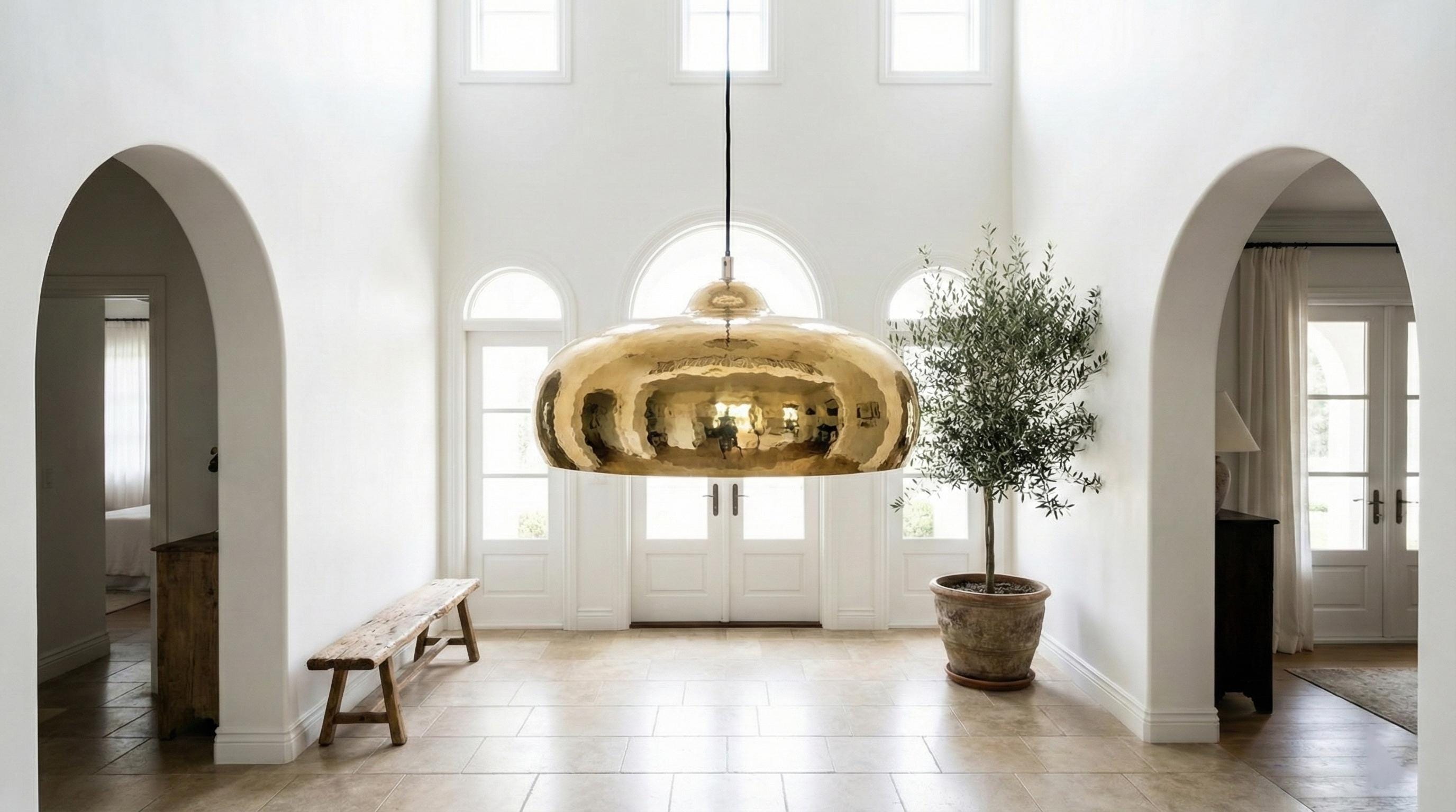 Modern interior with a gold pendant light, potted plant, and arched doorways.