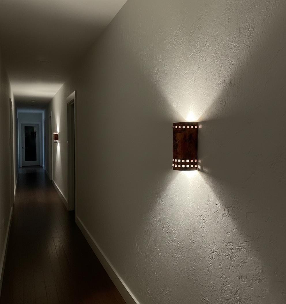 Wall-mounted light fixture casting a shadow on a wall in a dimly lit hallway.