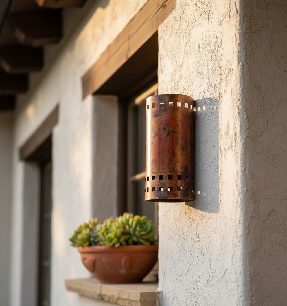 Decorative outdoor wall light fixture on a stucco wall with a plant below.