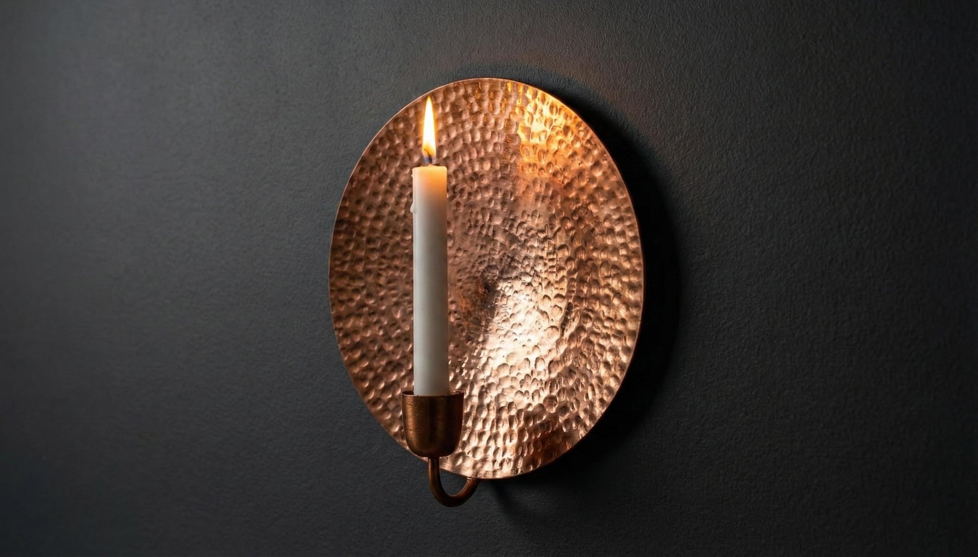 Copper wall sconce with a lit candle on a dark background