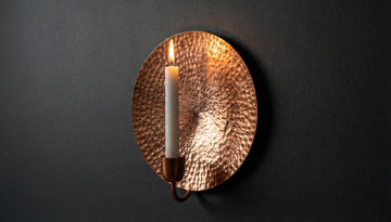 Copper wall sconce with a lit candle on a dark background