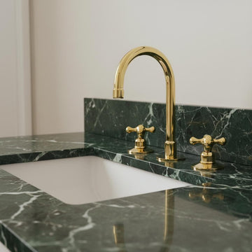 Gold faucet on a green marble countertop with a white sink.