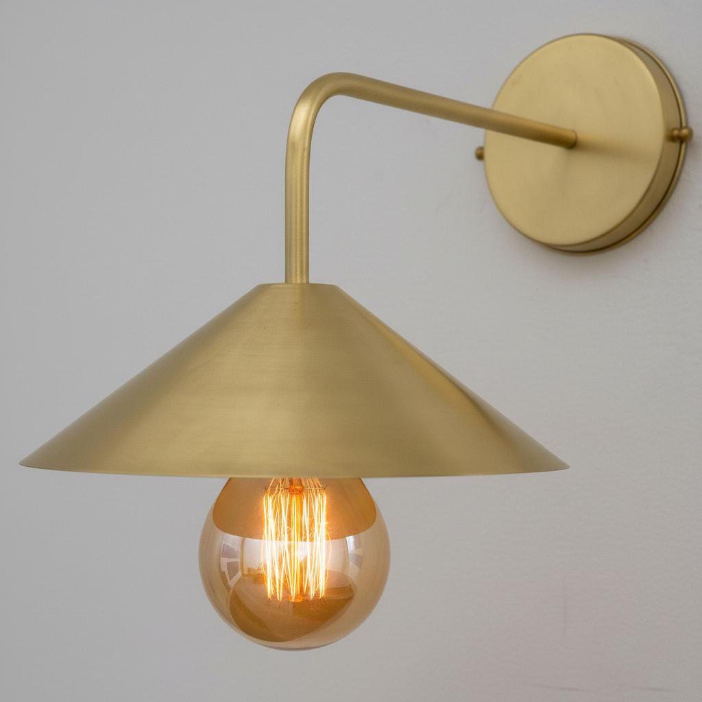 Gold wall-mounted lamp with a visible light bulb against a gray background