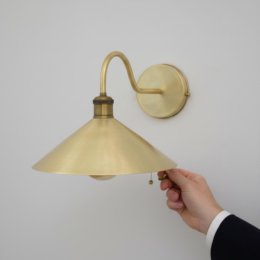 Brass wall sconce with a hand adjusting the light switch against a plain background