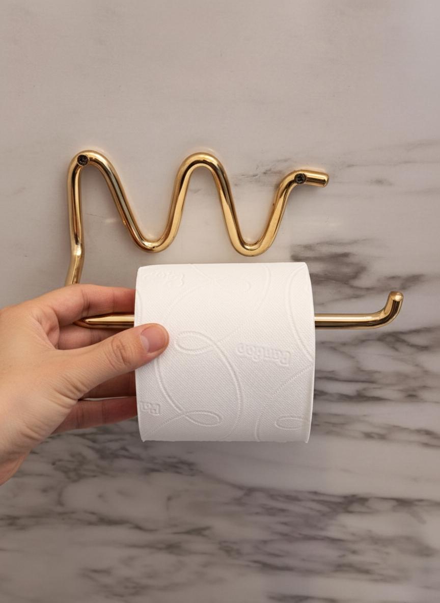 Gold toilet paper holder with a roll of toilet paper against a marble wall.