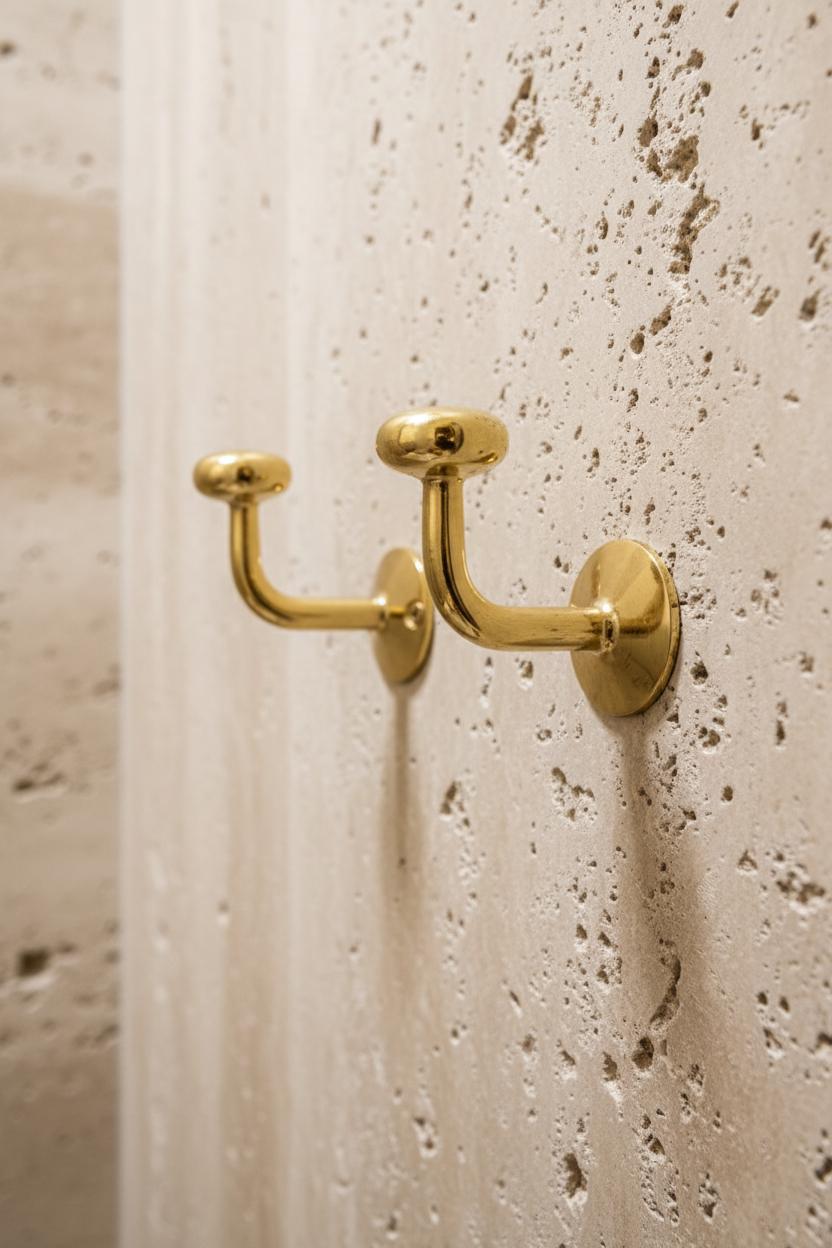 Gold double hook mounted on a textured beige wall