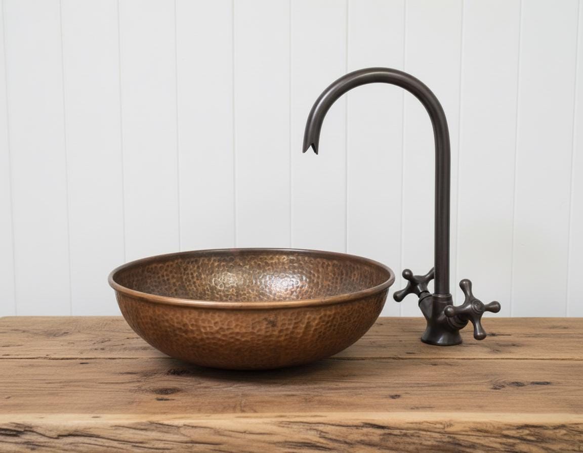 Copper sink and faucet on a wooden surface with a white paneled background