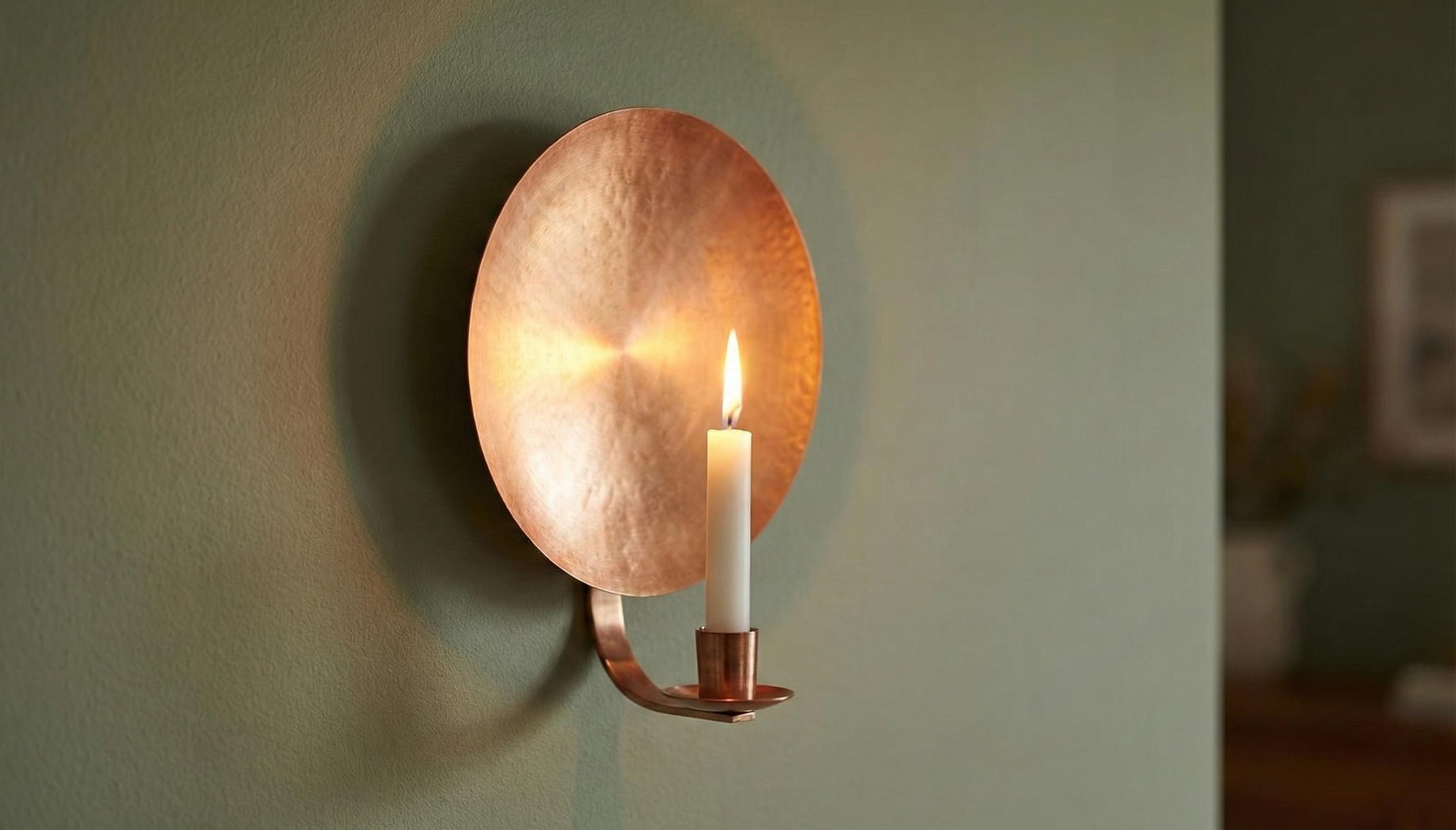 Copper wall sconce with a lit candle on a neutral background