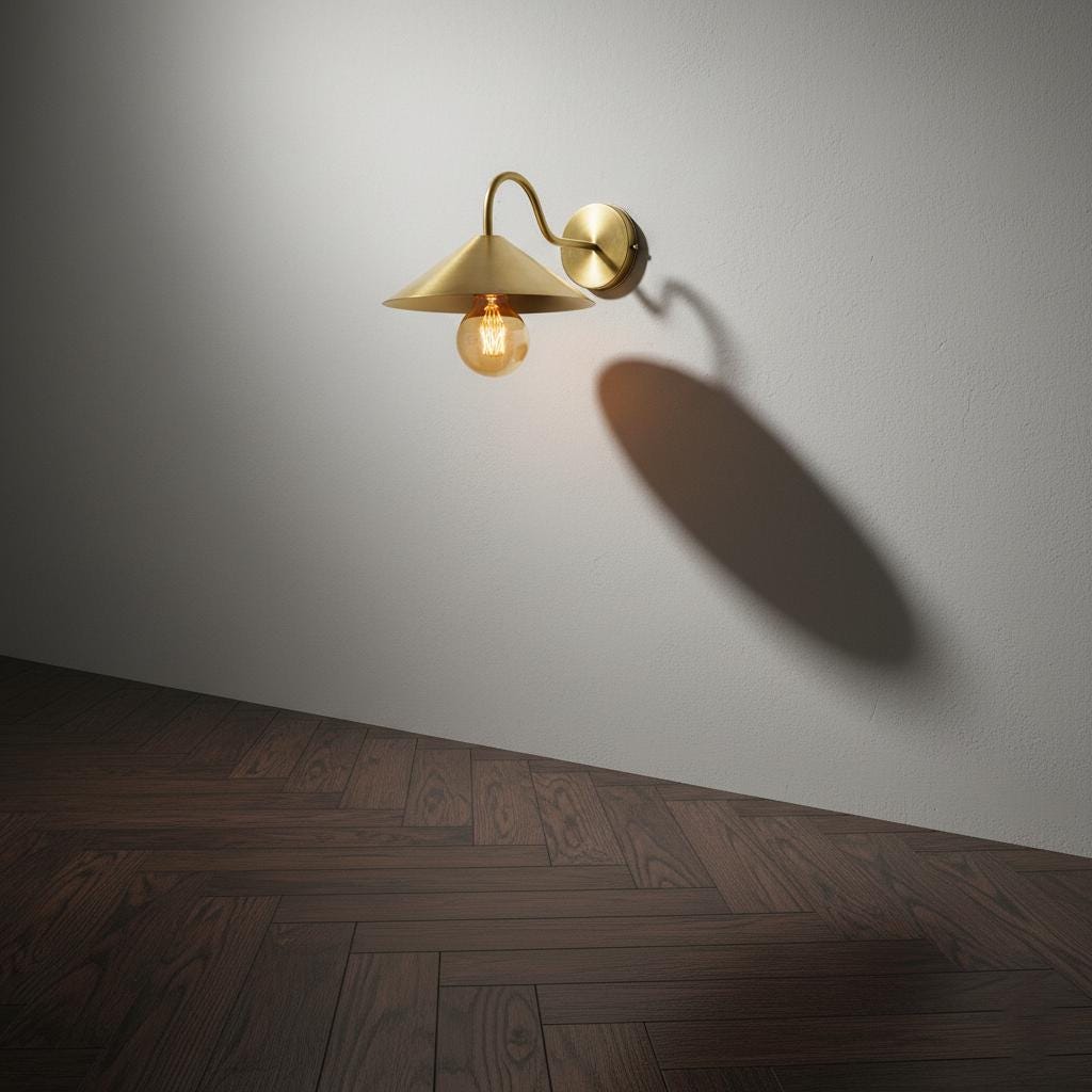 Gold wall-mounted lamp casting a shadow on a gray wall with wooden floor.