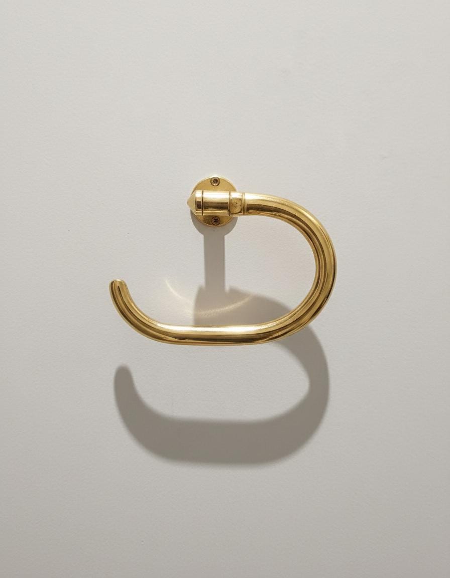 Gold toilet paper holder with a roll of toilet paper on a light gray wall.