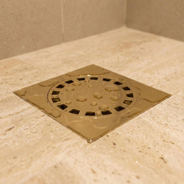Metallic shower drain cover on a tiled bathroom floor