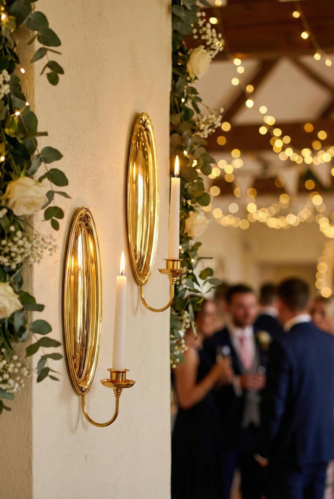 Two gold wall sconces with lit candles on a light gray wall.