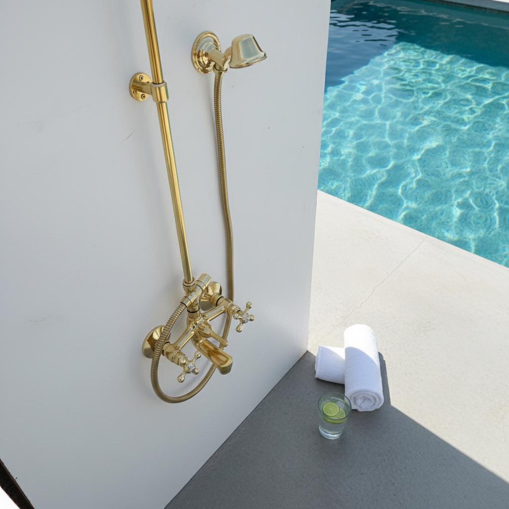 Gold shower system next to a pool with a glass of water and towel on a ledge.