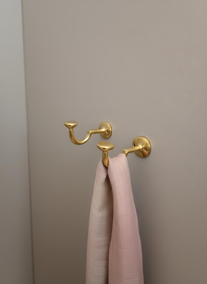 Gold double hook with a pink towel on a beige wall