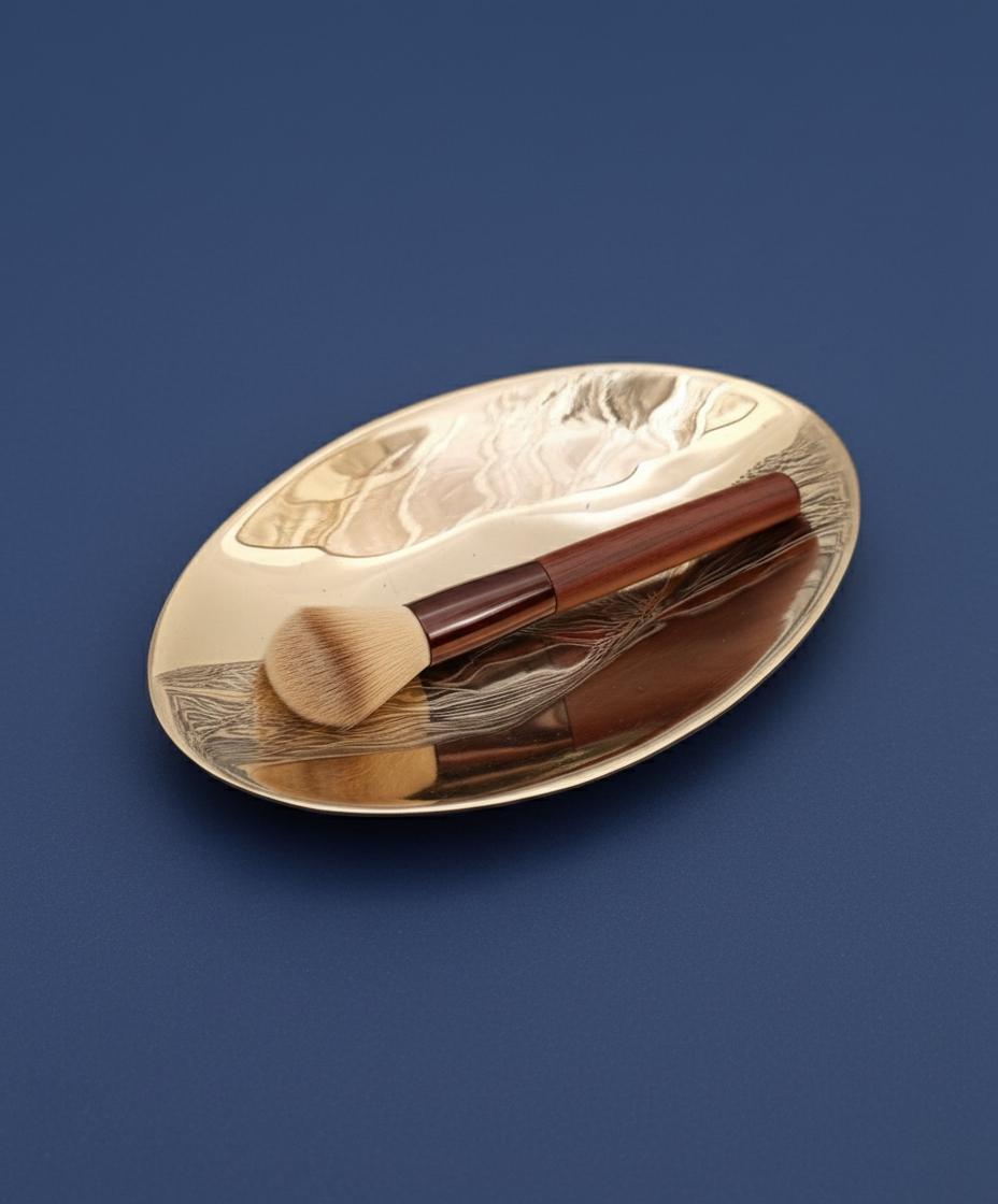 Makeup brushes on a decorative gold and brown oval dish against a blue background