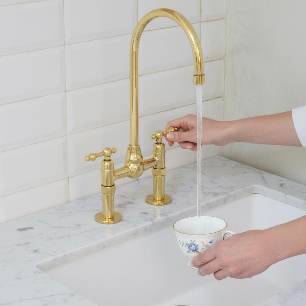 Gold kitchen faucet with a person filling a teacup from it.