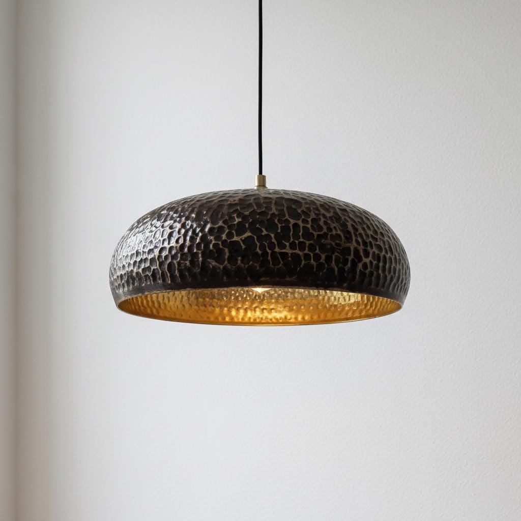 Hammered metal pendant light with gold interior on a plain background