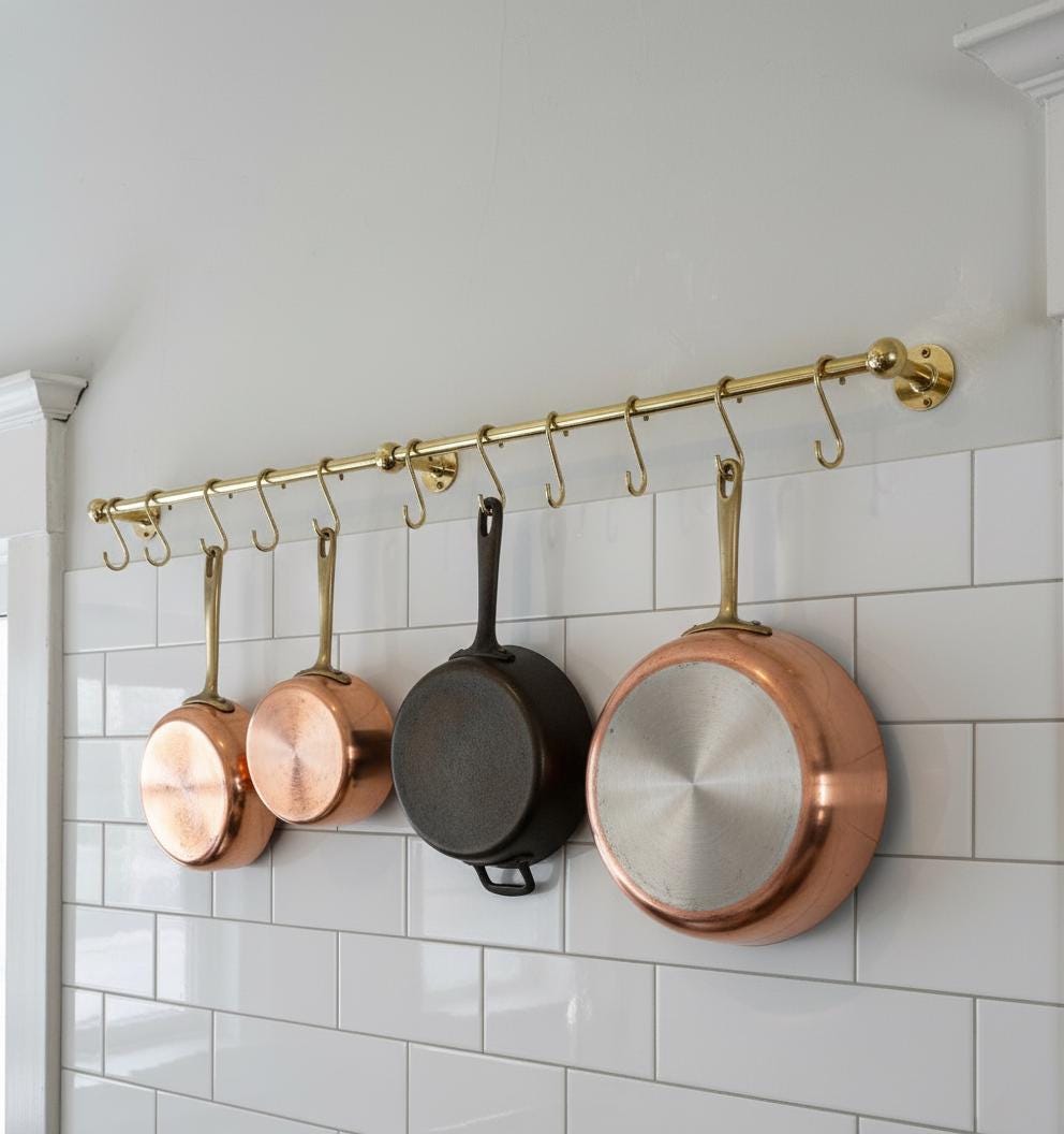Copper and black pans hanging on a gold pot rack against a white tiled wall.