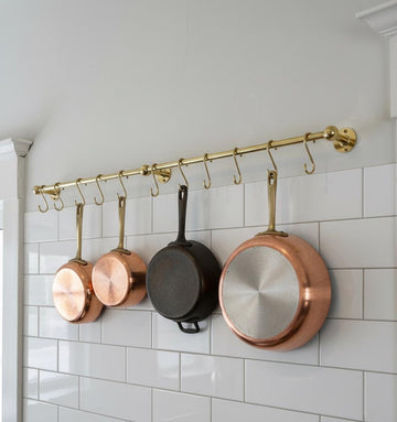 Copper and black pans hanging on a gold pot rack against a white tiled wall.