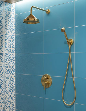 Gold shower head and control valve on a blue tiled wall with decorative corner tile.