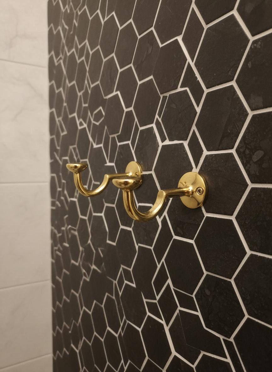 Gold double hook on a black hexagonal tiled wall