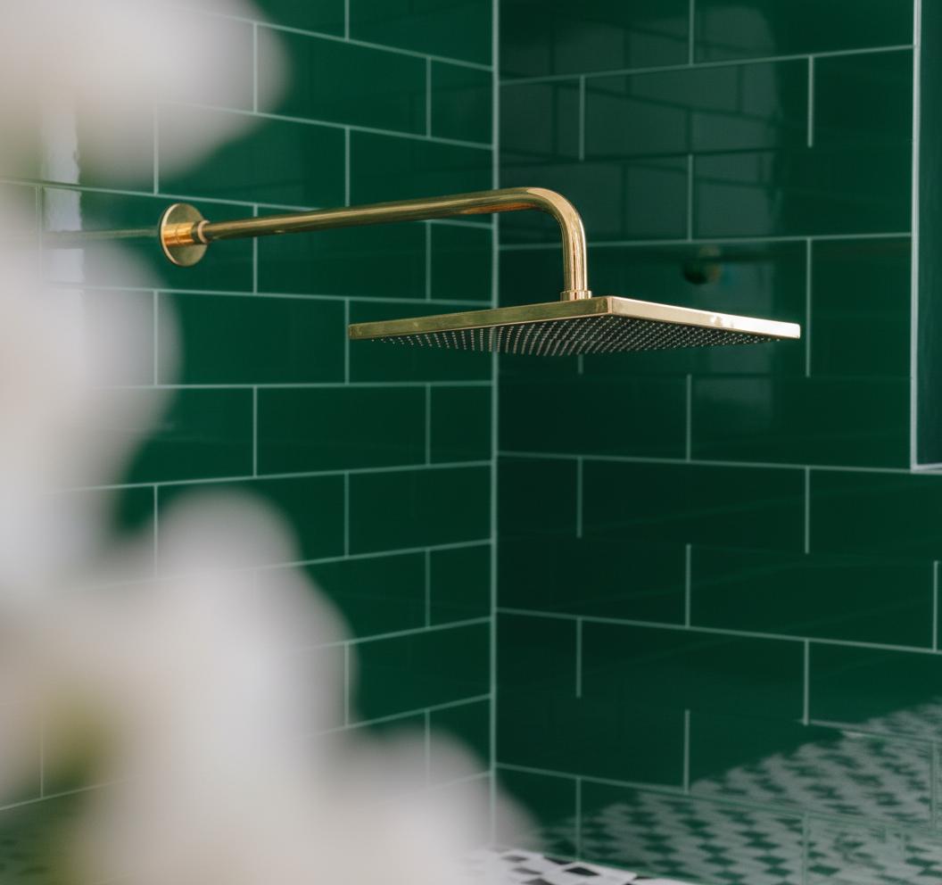 Gold shower head mounted on a green tiled wall